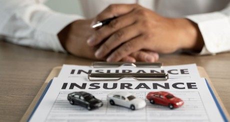 A person sitting behind car insurance forms with car toys on them | Why It Pays to Compare Auto Insurance Rates Every Year